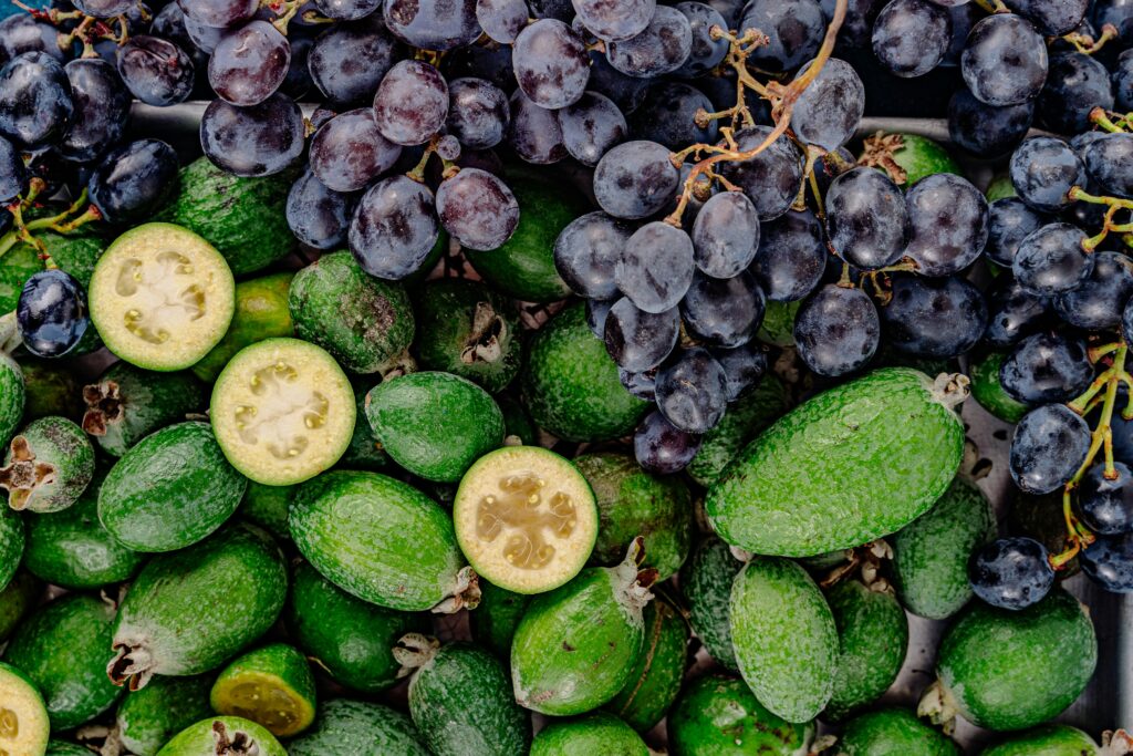 Vibrant display of fresh feijoa and grapes, showcasing a top view of green and dark purple fruits for a healthy lifestyle.